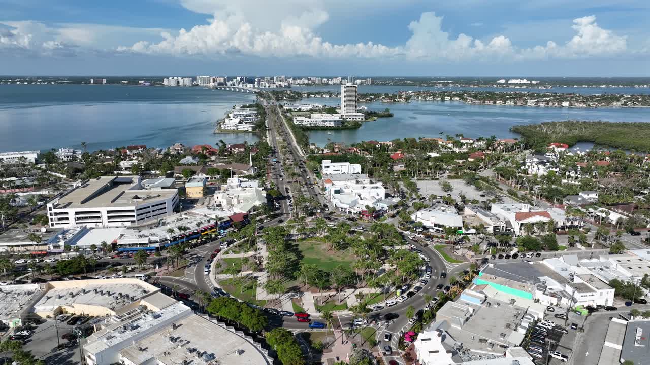 St Armands Circle Roundabout with traffic and bridge during sunny day. Aerial top down shot. Sarasota City, Florida, USA. Wide shot. Palm trees in iconic district. Gulf of Mexico and America.