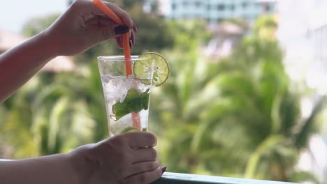 glass-stands-on-balcony-railing-and-girl-stirs-cocktail