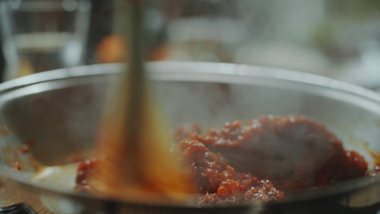 primer plano del uso de la espátula para agitar la salsa de tomate humeante en la sartén