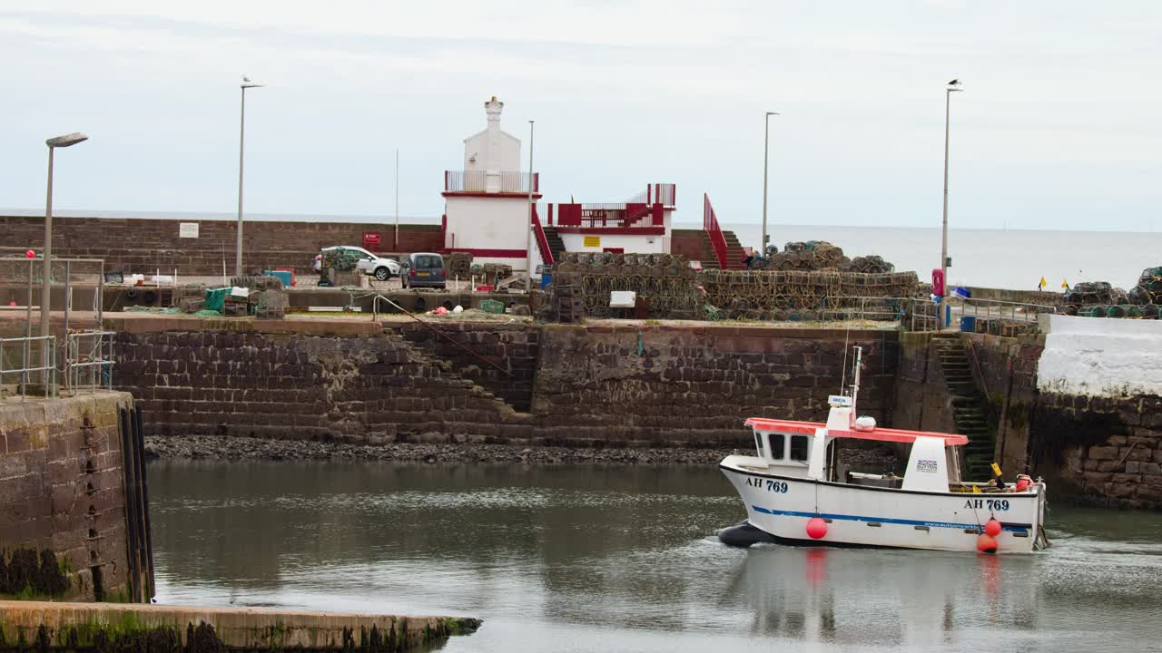 Small fishing boat moves through calm harbor waters, overcast daylight, static wide shot, coastal setting
