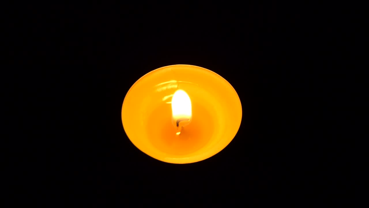 La candela tremola nel buio. Una candela bianca e rotonda brucia su uno sfondo scuro. Candele rotonde bruciano e si spengono. Dolore. Romanticismo. Gioia. Video 4K.