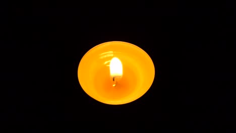 la vela parpadea en la oscuridad. una vela redonda blanca arde sobre un fondo oscuro. las velas redondas arden y se apagan. tristeza. romance. alegría. video 4k