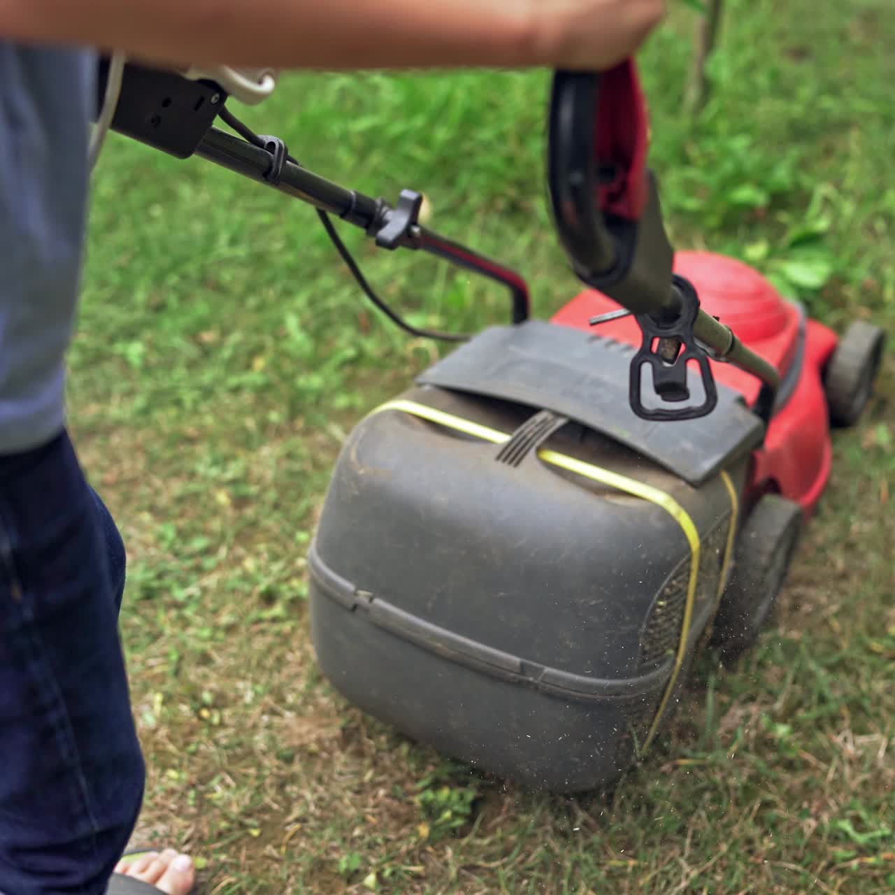 Red lawn mower in the garden. Boy is cutting grass by electrical mower machine outdoors.