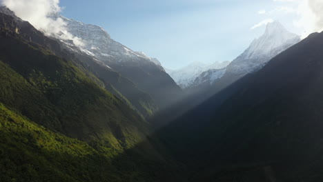 epic rotating aerial shot of the sun shining through the mountain onto a mountain face inside the annapurna mountains, nepal