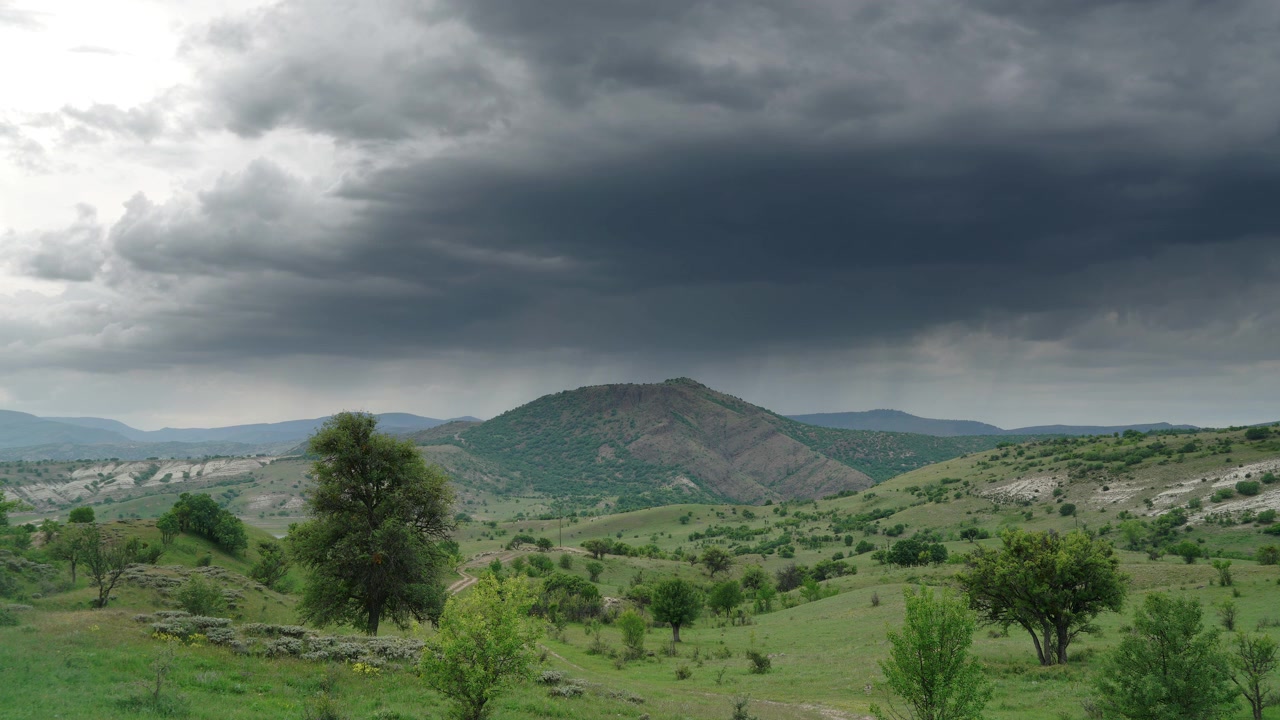 Nuvole tempestose che si addensano su verdi colline ondulate e un paesaggio montano