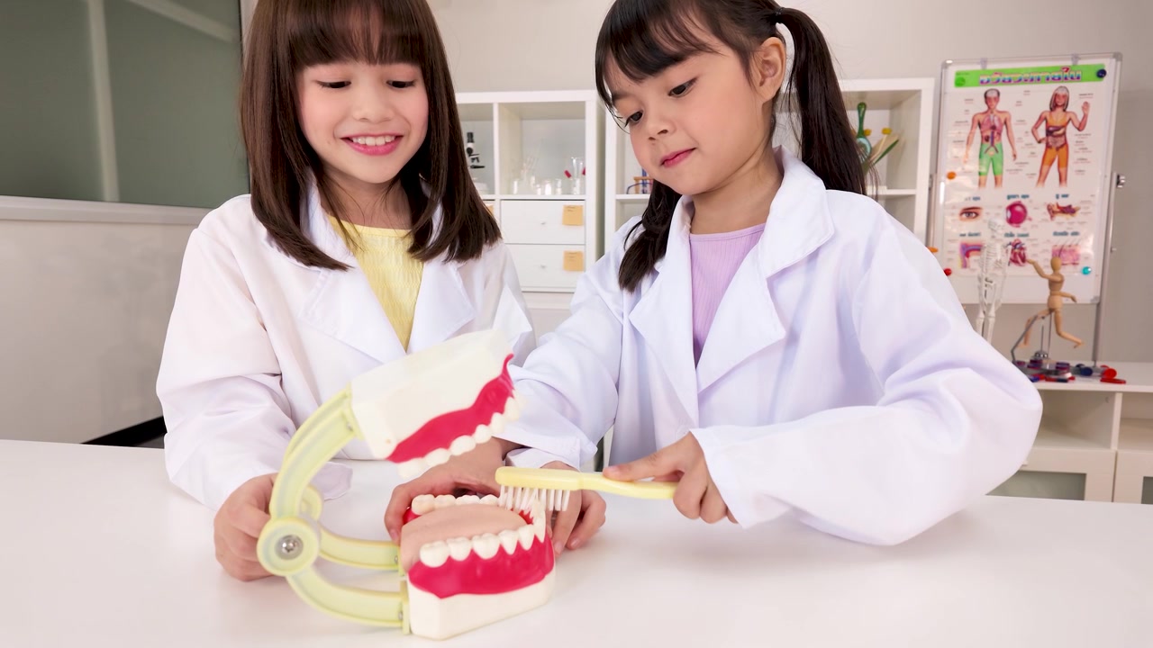 Hai sinh viên trẻ mặc áo blouse trắng dùng bàn chải đánh răng trên mô hình nha khoa trong lớp học.