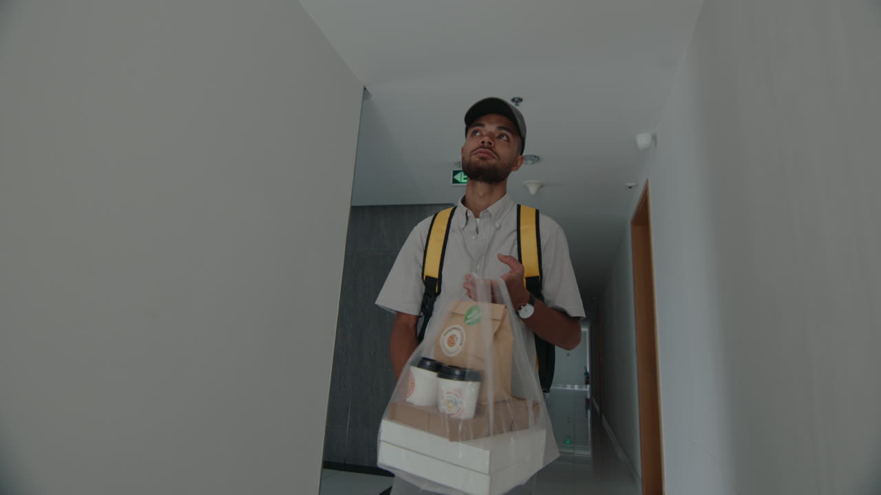 Young Male Courier Walking with Food along the Corridor