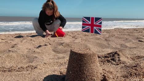 una niña llena un balde con arena para construir castillos de arena en una playa británica