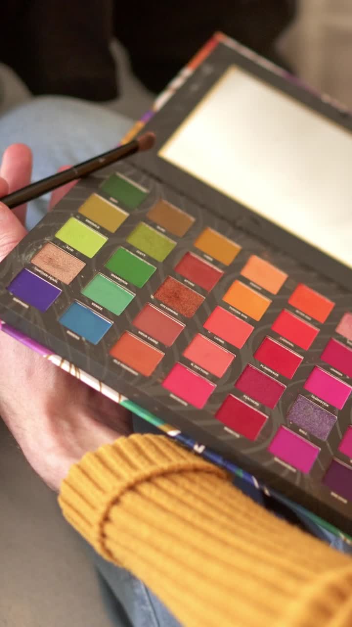 Close-up of a person holding a vibrant eyeshadow palette and makeup brush