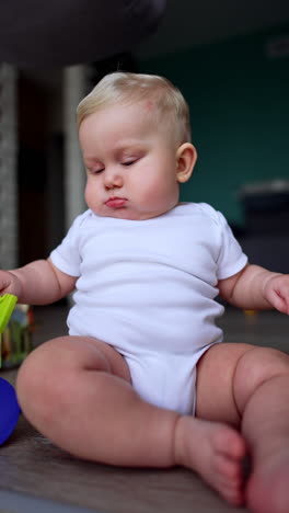 chubby blond baby boy in white bodysuit sits on the floor. little kid is focused on the kitchen brush. vertical video.