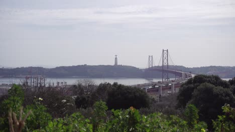 Time-lapse-of-the-Ponte-25-de-Abril-suspension-bridge-in-Lisbon-with-greenery-in-the-foreground