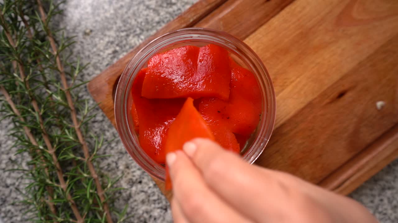 manos colocando pimientos asados picados en un frasco con aceite