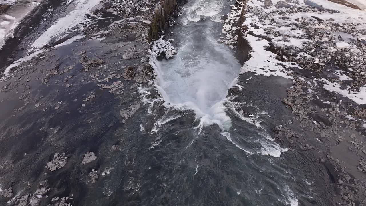 Selfoss waterfall aerial view in Iceland, snowy volcanic cliffs, icy river plunge into rugged canyon, stunning winter landscape.