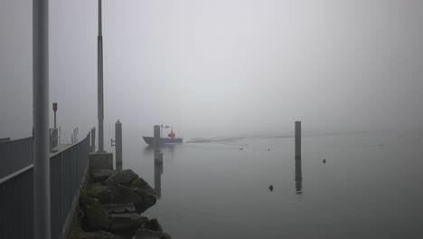 a small boat with one orange dressed guy drives from the right to the left out of the haze