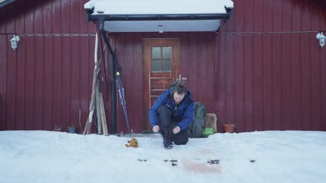 man tying boots in front of his cabin at winter