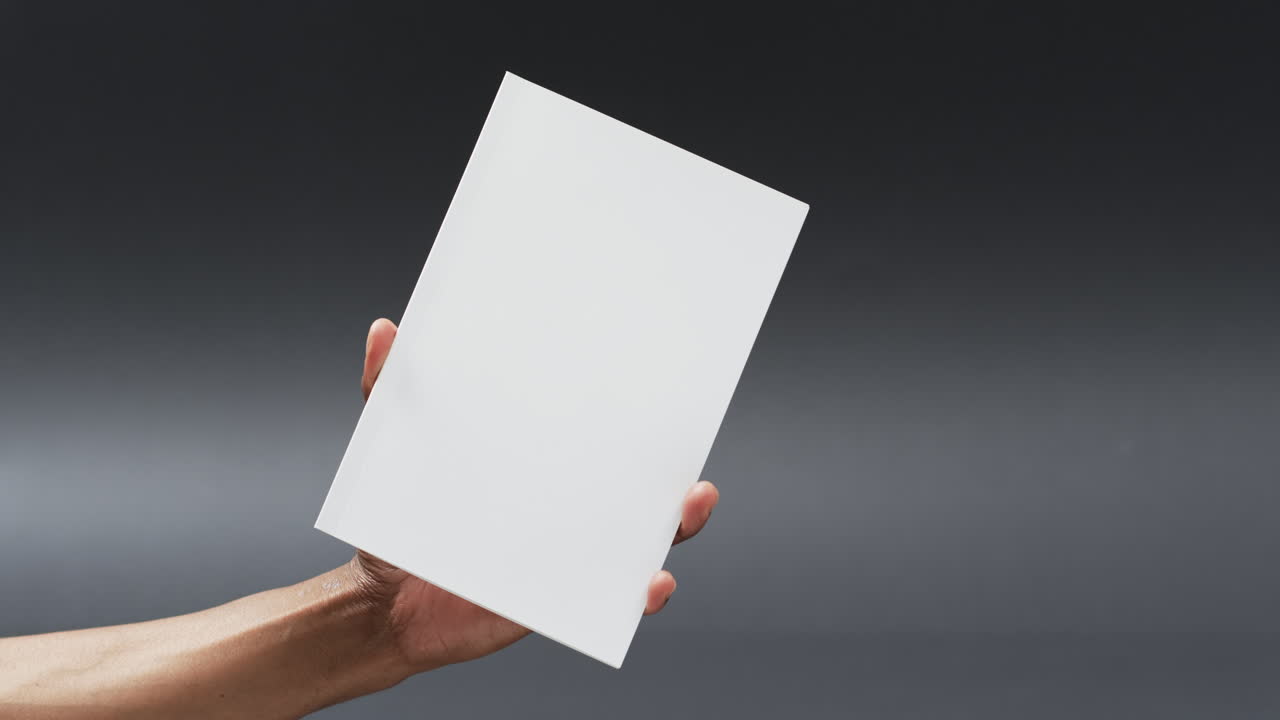 Video of hand of african american man holding book with blank page, copy space on grey background