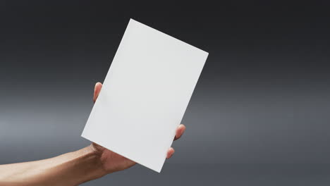 video of hand of african american man holding book with blank page, copy space on grey background