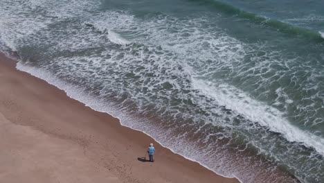 Drone-Pan-Sobre-Pescador-Masculino-Ajustando-La-Caña-De-Pescar-En-La-Costa-áspera-De-Cape-Cod