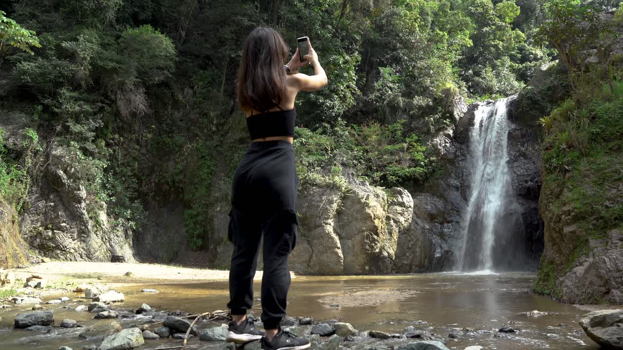 Young women making a phone video of a waterfall in the insides of a Caribbean island forest