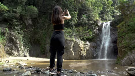 young women making a phone video of a waterfall in the insides of a caribbean island forest
