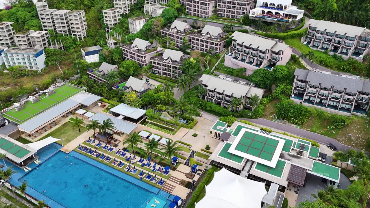 Drone footage captures a sprawling resort in Phuket, Thailand, showcasing lush greenery, pools, and modern architecture under bright daylight