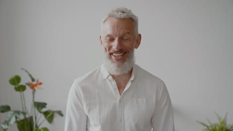 senior man with gray hair and white shirt looking at camera laughing