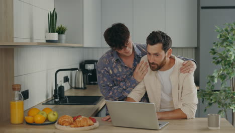 happy gay couple using laptop in kitchen