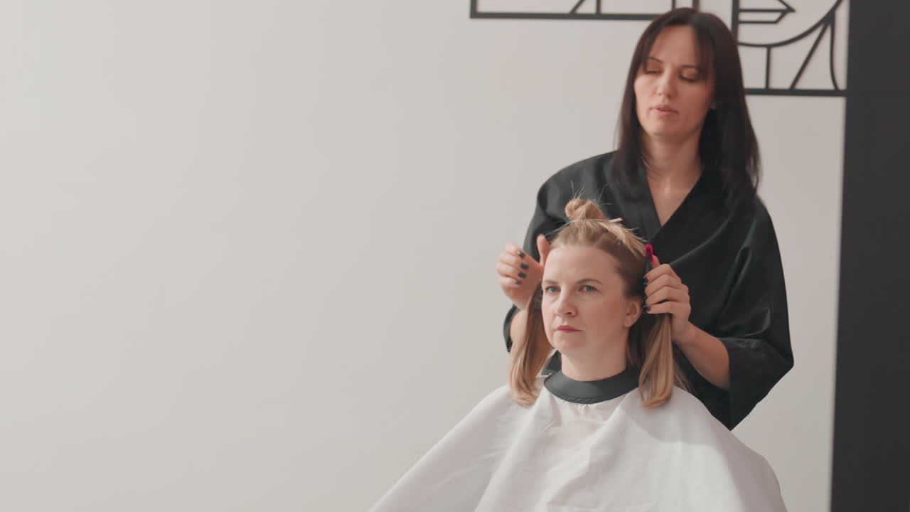 Donna che si fa tagliare i capelli in un salone. L’hairstylist divide i capelli all’altezza delle spalle con clip e forbici, la cliente indossa una mantellina protettiva, studio bianco minimalista, hairstylist concentrato/a a creare un taglio preciso