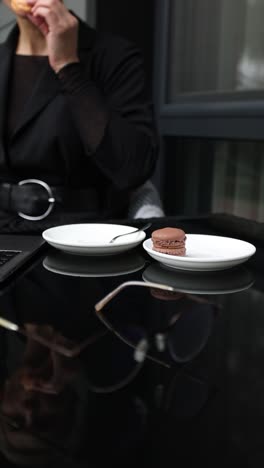 woman eating macarons at a cafe while working on her laptop