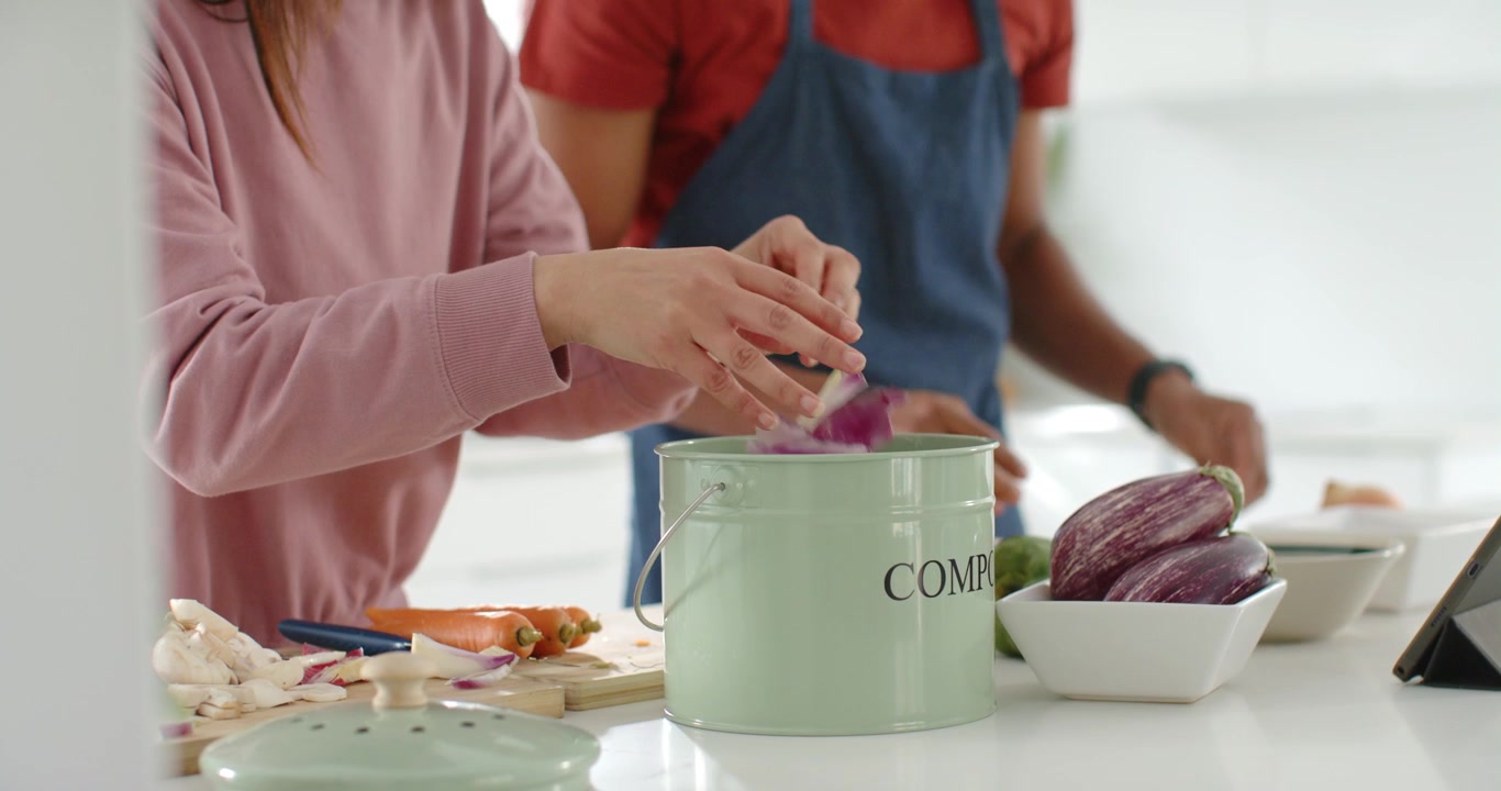 Coppia africana che inizia la preparazione della cena al bancone, tagliando verdure e aggiungendo gli scarti nel bidone del compost.