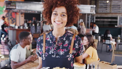portrait of waitress serving food in busy bar restaurant smiling at camera