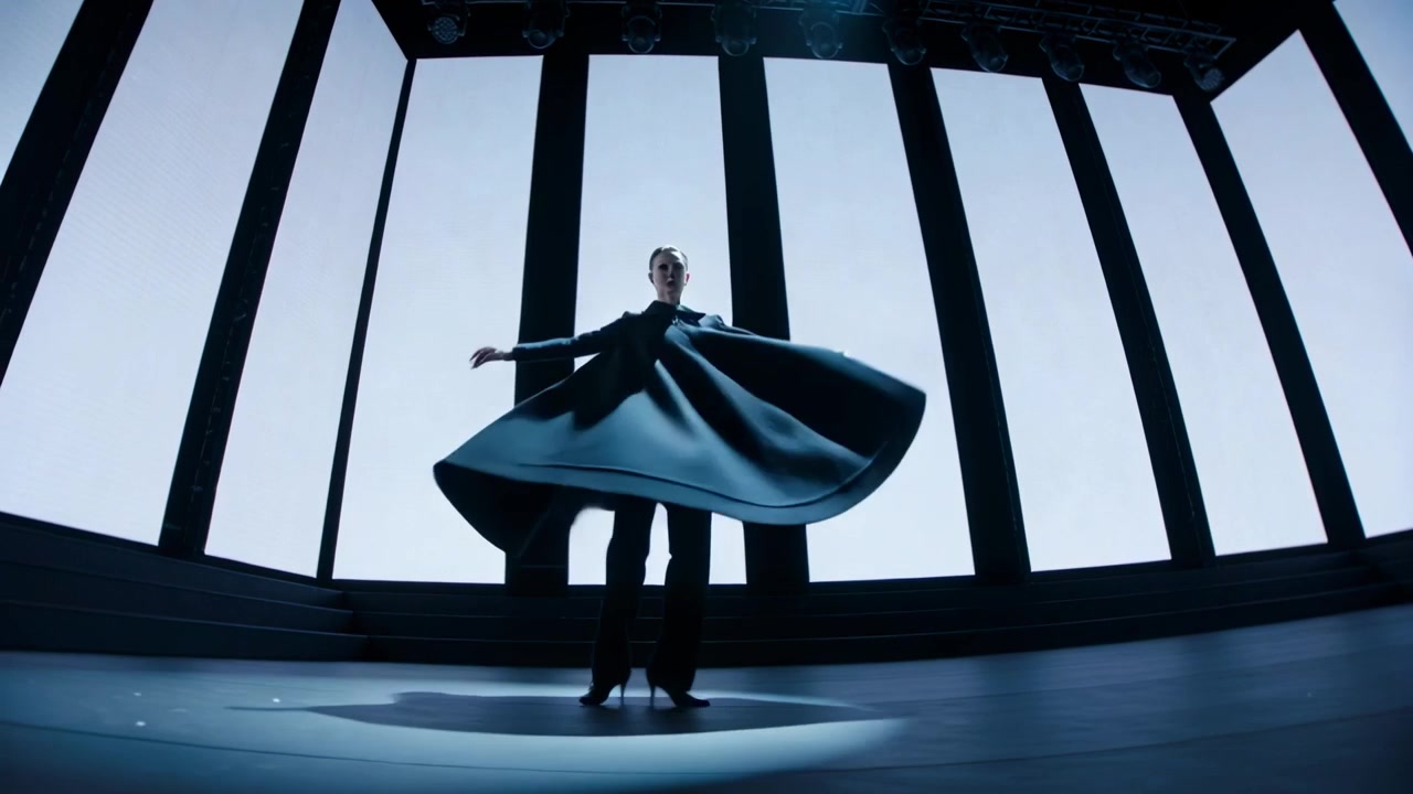Kvindelig performer drejer rundt og reagerer på spotlight, drejer på scenen i høje hæle og en flagrende mørk kappe