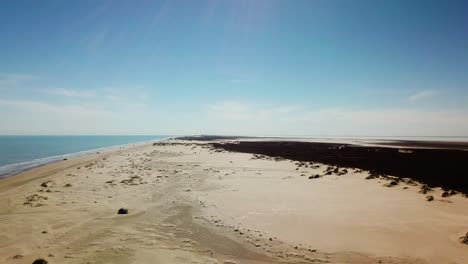 Drone---rising,-reveal-view-of-the-shoreline-and-sand-dunes-on-a-gulf-coast-barrier-island-on-a-sunny-afternoon,-fisherman-and-vehicles-in-the-distance---South-Padre-Island,-Texas