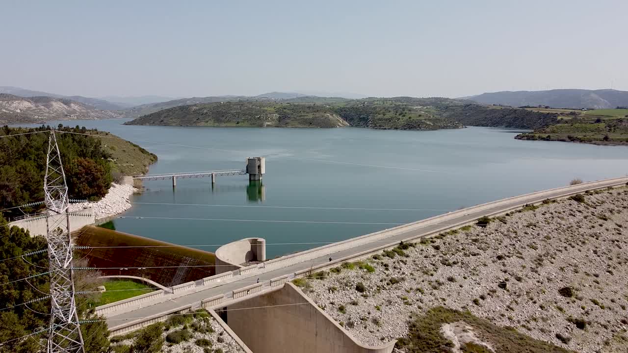 This stunning location showcases a large dam sitting beside a serene body of water, bordered by lush green hills under a clear sky. Perfect for nature lovers and photographers