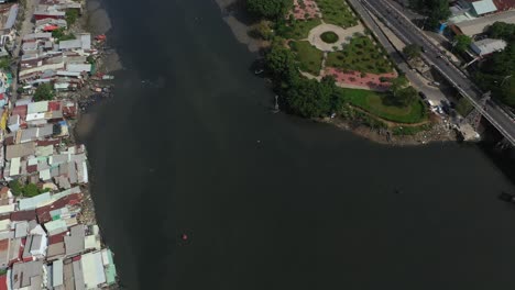 Drone-flight-over-Kenh-Te-canal-in-Ho-Chi-Minh-City-Vietnam-on-sunny-afternoon-with-river-boats,-waterfront-houses-and-landscaped-park