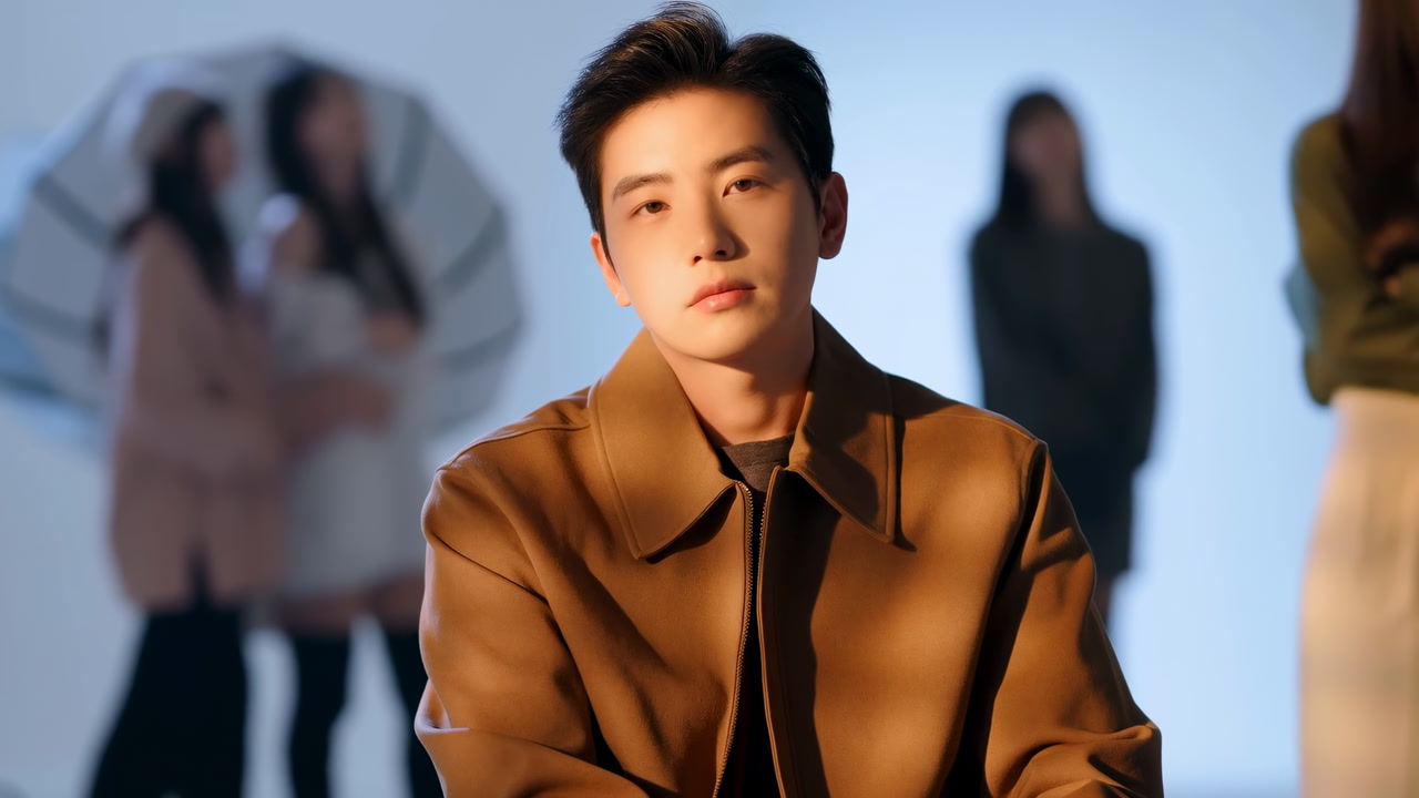 East Asian Actor Seated In Studio, Cinematic Portrait With Warm Brown Coat, Soft Key Lighting, Blurred Female
