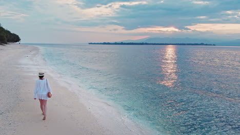 beautiful caucasian woman on vacation walking along tropical sandy beach during golden sunrise