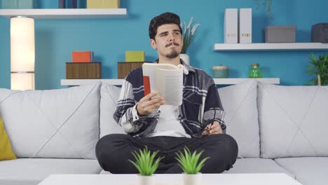 un joven con gafas está leyendo un libro en casa.