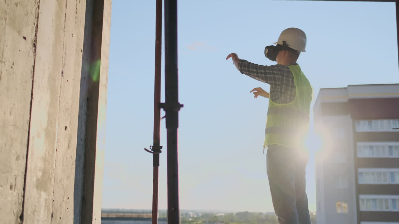Engineer Builder visualizes the building plan standing on the roof of the building at sunset stands in VR glasses and moves his hands using the interface of the future. Futuristic engineer of the future. The view from the back.