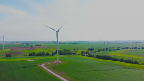 Countryside-renewable-energy-wind-turbines-on-flat-green-pastoral-farm-land-on-sunny-day,-aerial-approach