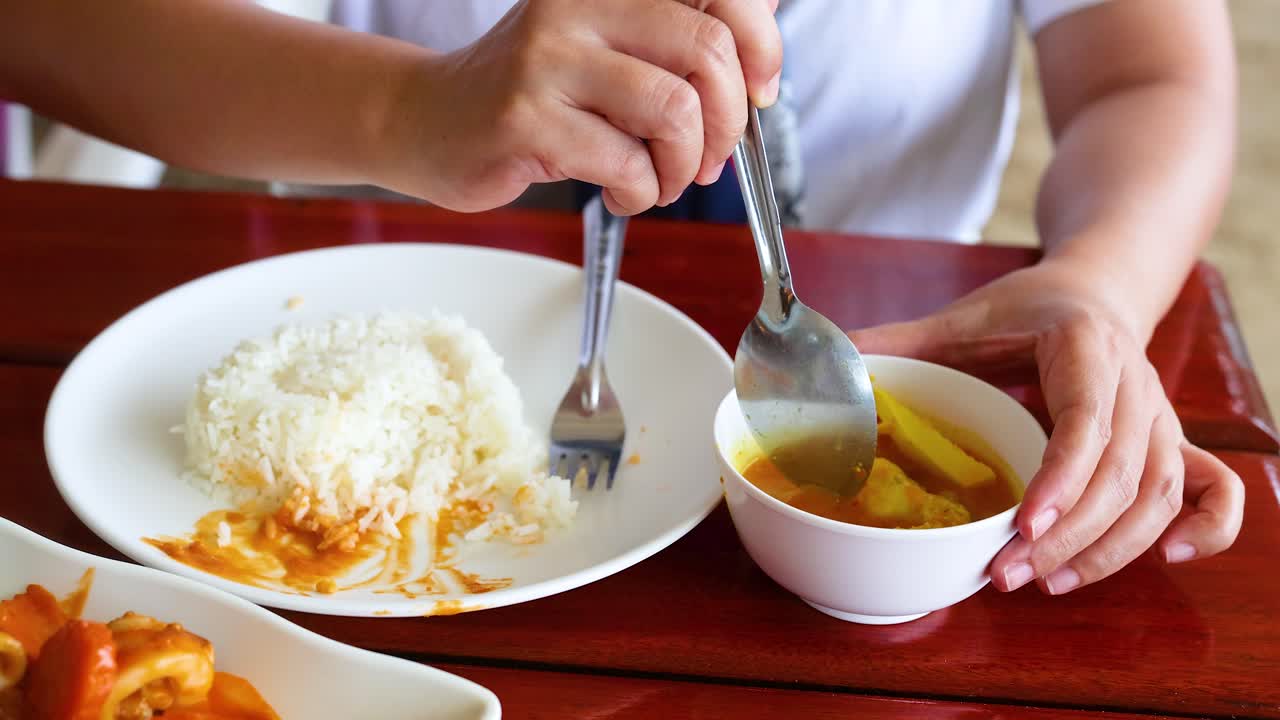 한 사람이 과 함께 전통적인 태국 커리 요리를 즐기며, 활기찬 색상과 진정한 맛을 편안한 환경에서 보여줍니다.