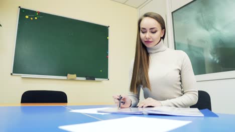 student doing homework in the classroom at the table on the background of the chalkboard