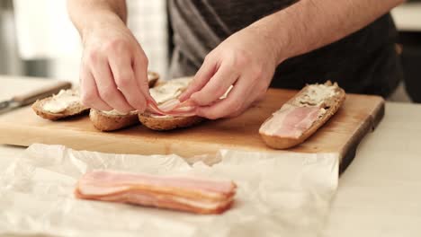 Hombre-Caucásico-Colocando-Cuidadosamente-Tiras-De-Tocino-En-Baguette-En-Rodajas-En-La-Cocina