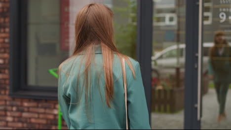 woman in jacket walks towards glass door of shop building