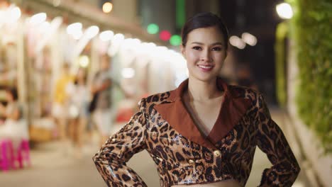 beautiful asian girl with stunning and alluring smile looks at the camera and poses in the city at night