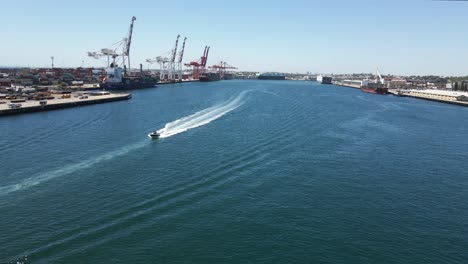 una toma aérea dinámica de un puerto marítimo que se mueve hacia las grúas mientras pasa sobre un bote rápido en el agua