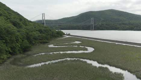 드론은 작은 휘어지는 하천을 찍고, 앞으로 이동하고 위로 어, 배경에 다리를 드러니다.