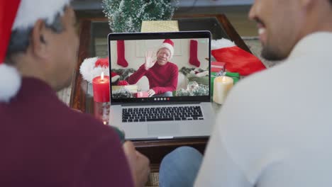 Smiling-biracial-father-and-son-using-laptop-for-christmas-video-call-with-man-on-screen