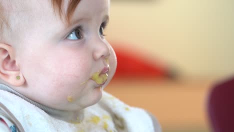 después de tomar un bocado de comida para bebés de su madre, el bebé mira a su madre con comida todavía en la cara, primer plano