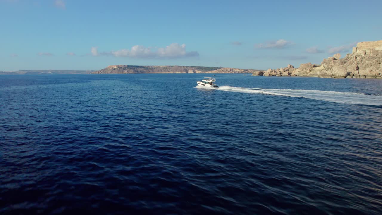 Low FPV aerial shot following a fast motorboat moving across the deep blue sea near Malta’s rocky coastline under a bright clear sky